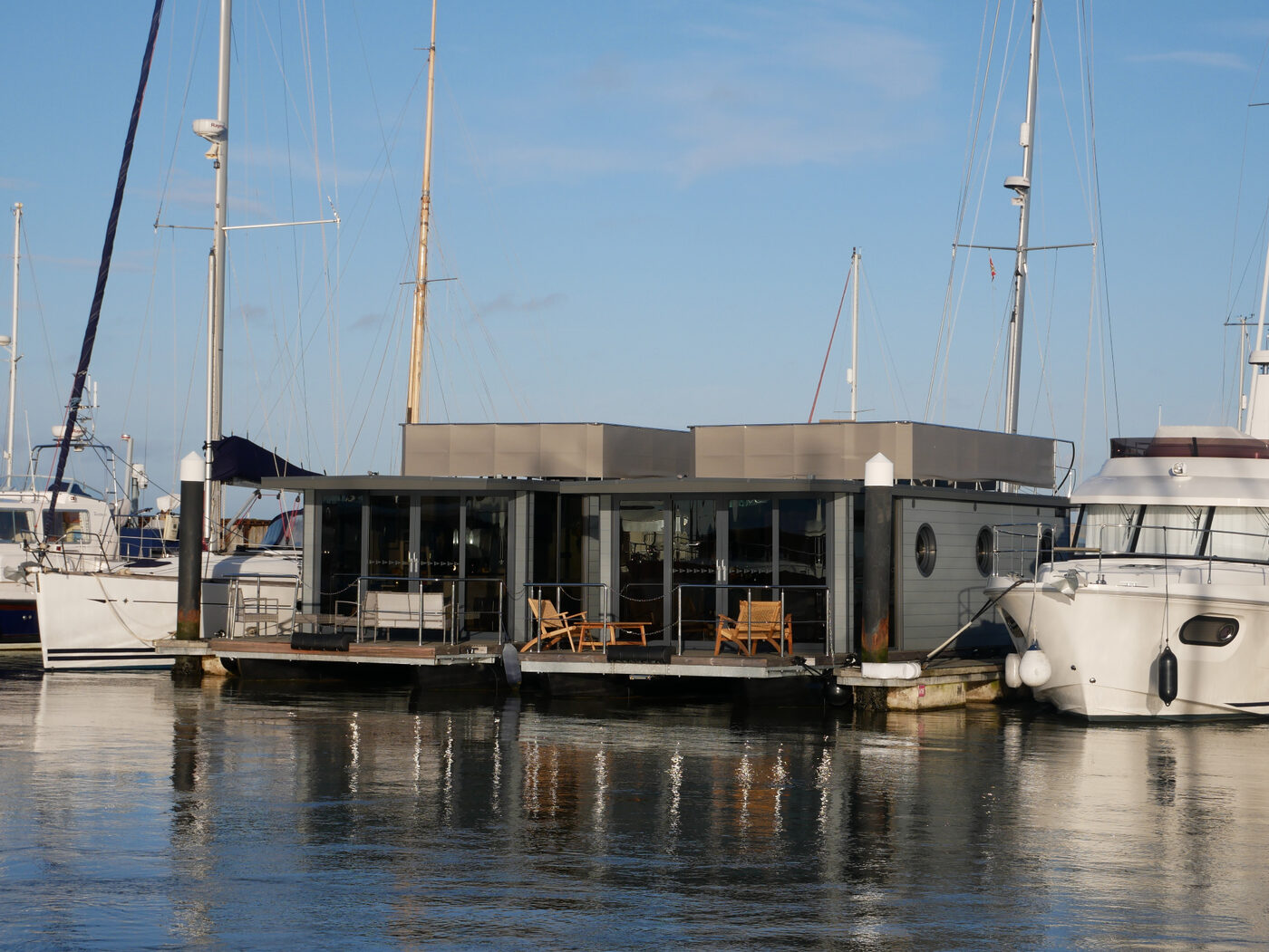 Modern self-catering houseboat with sea-facing deck moored among yachts in Yarmouth Harbour marina