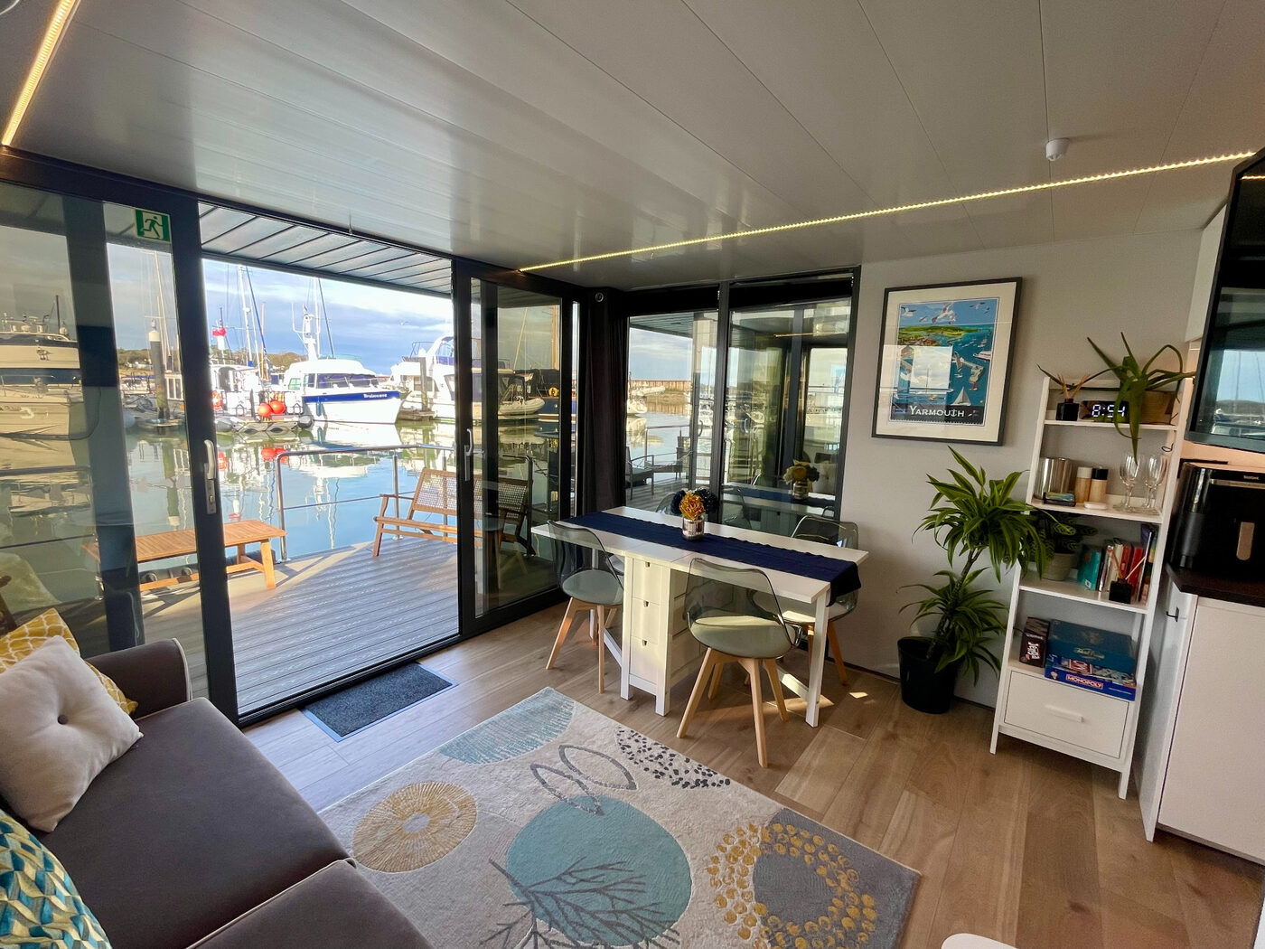 Bright open-plan living and dining area inside a Yarmouth Waterlodge houseboat with full-height glass doors opening onto the marina